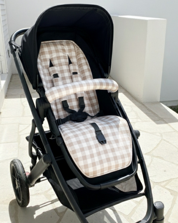 Black stroller with a beige checkered seat cover on a tiled floor.