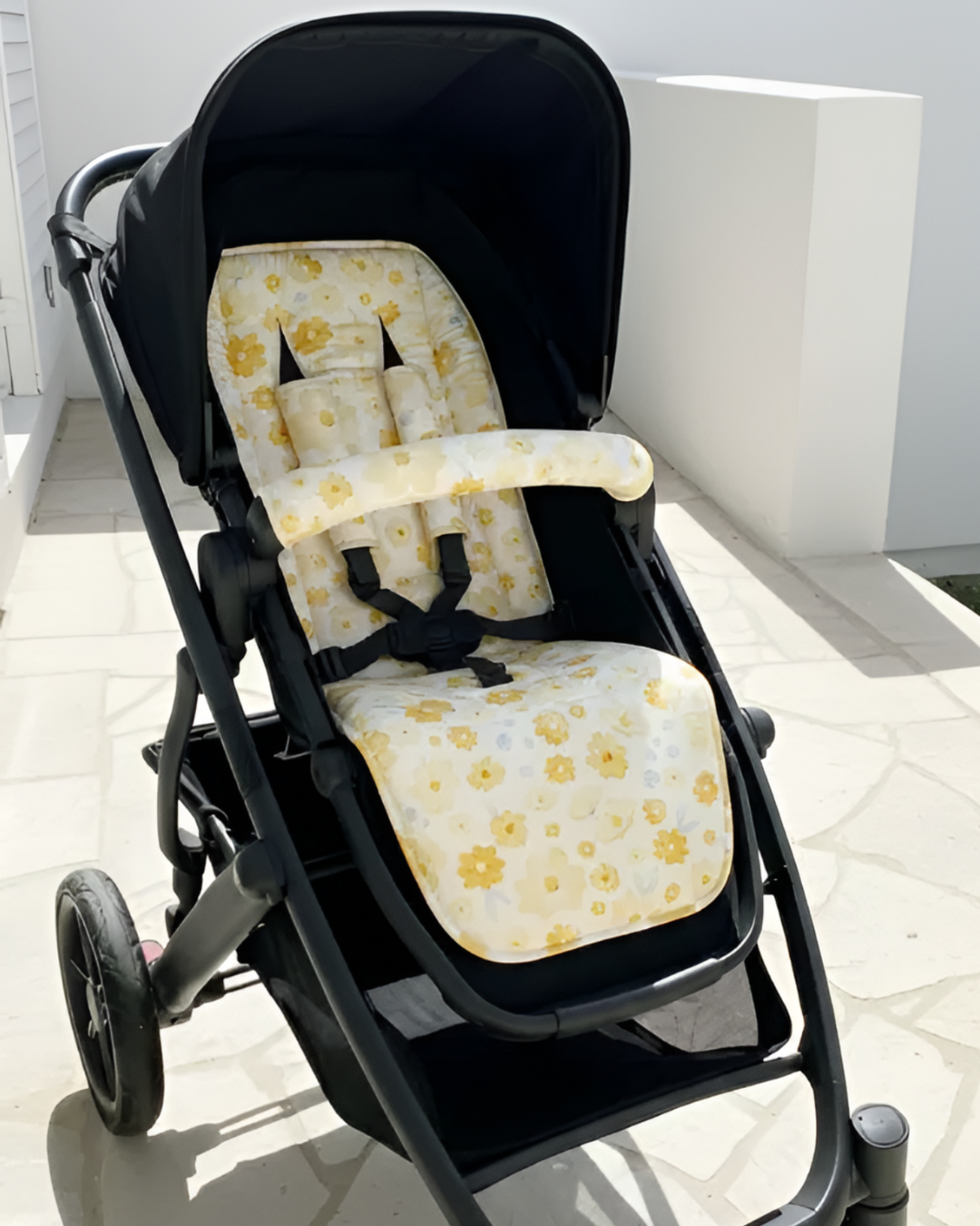 Black stroller with yellow floral cushion on a white floor