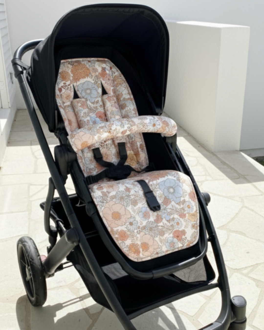 Floral-patterned baby seat cover on a stroller outdoors.