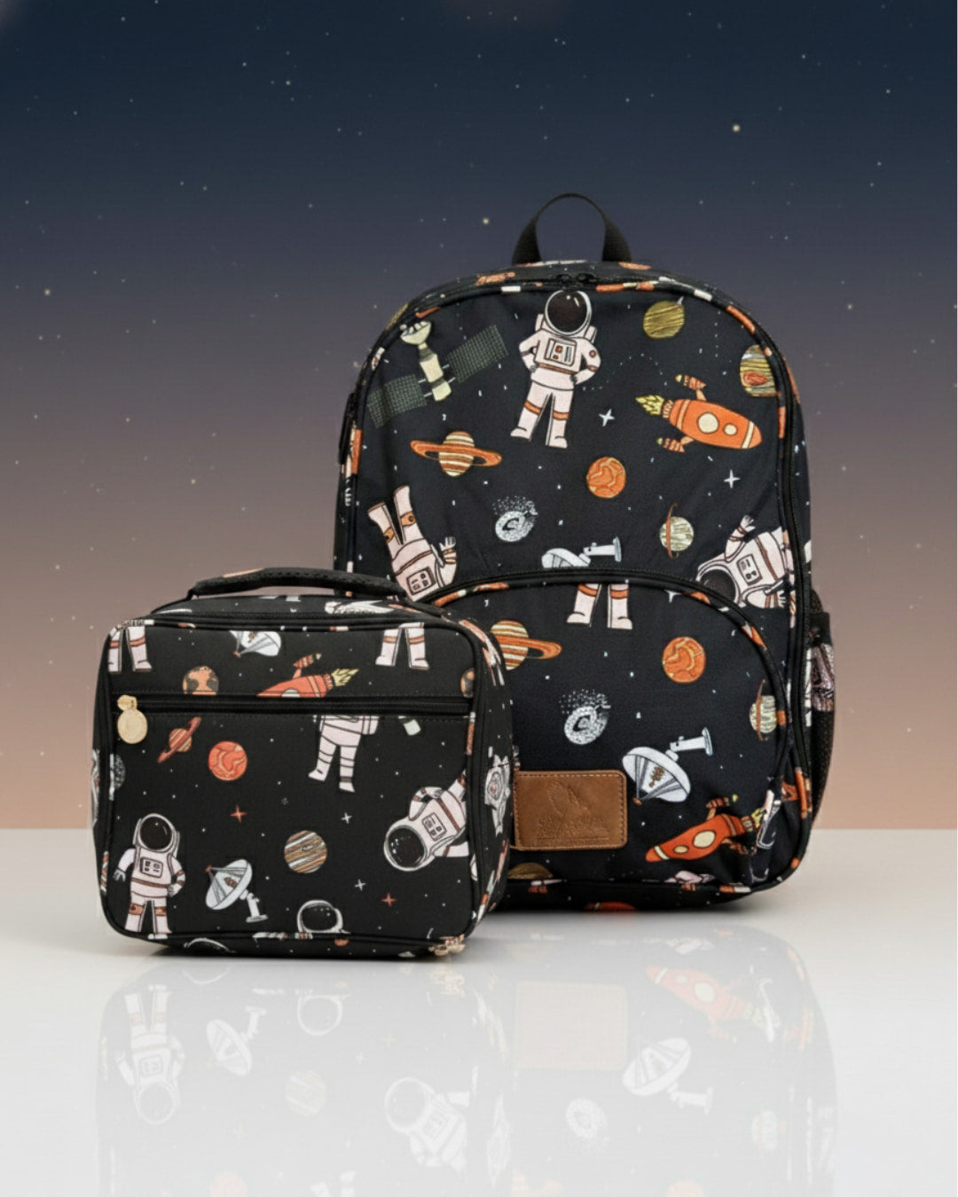 Backpack and lunch bag set with space-themed design on a reflective surface.