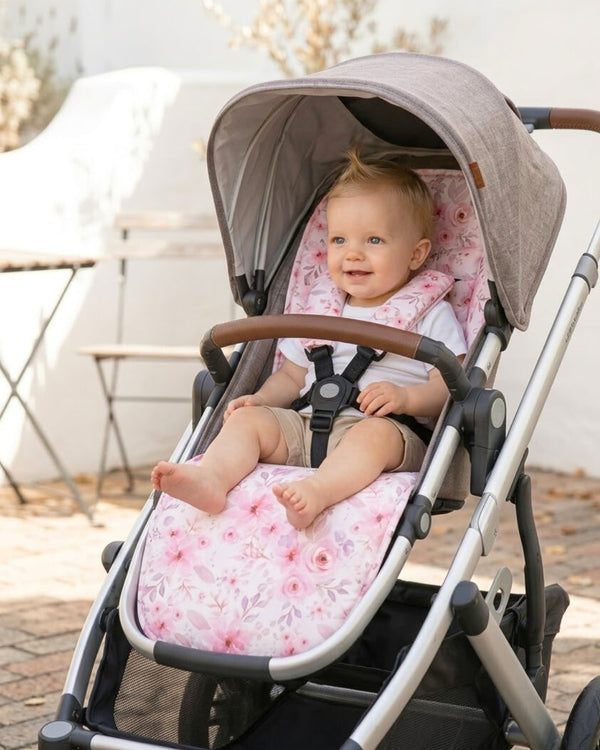 Baby girl sitting in a stroller with a floral seat cover, outdoors.