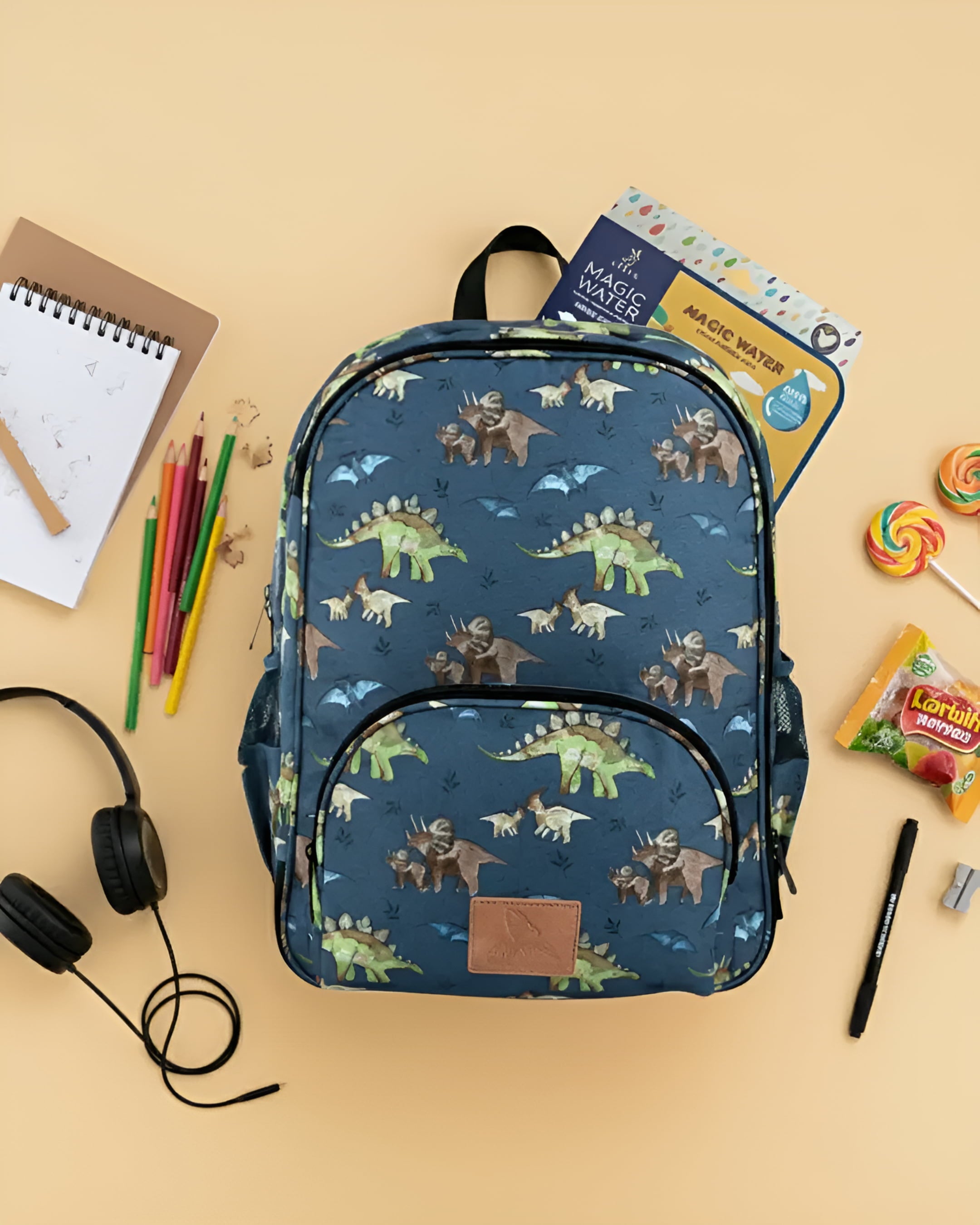 Backpack with dinosaur pattern on a beige background with school supplies.