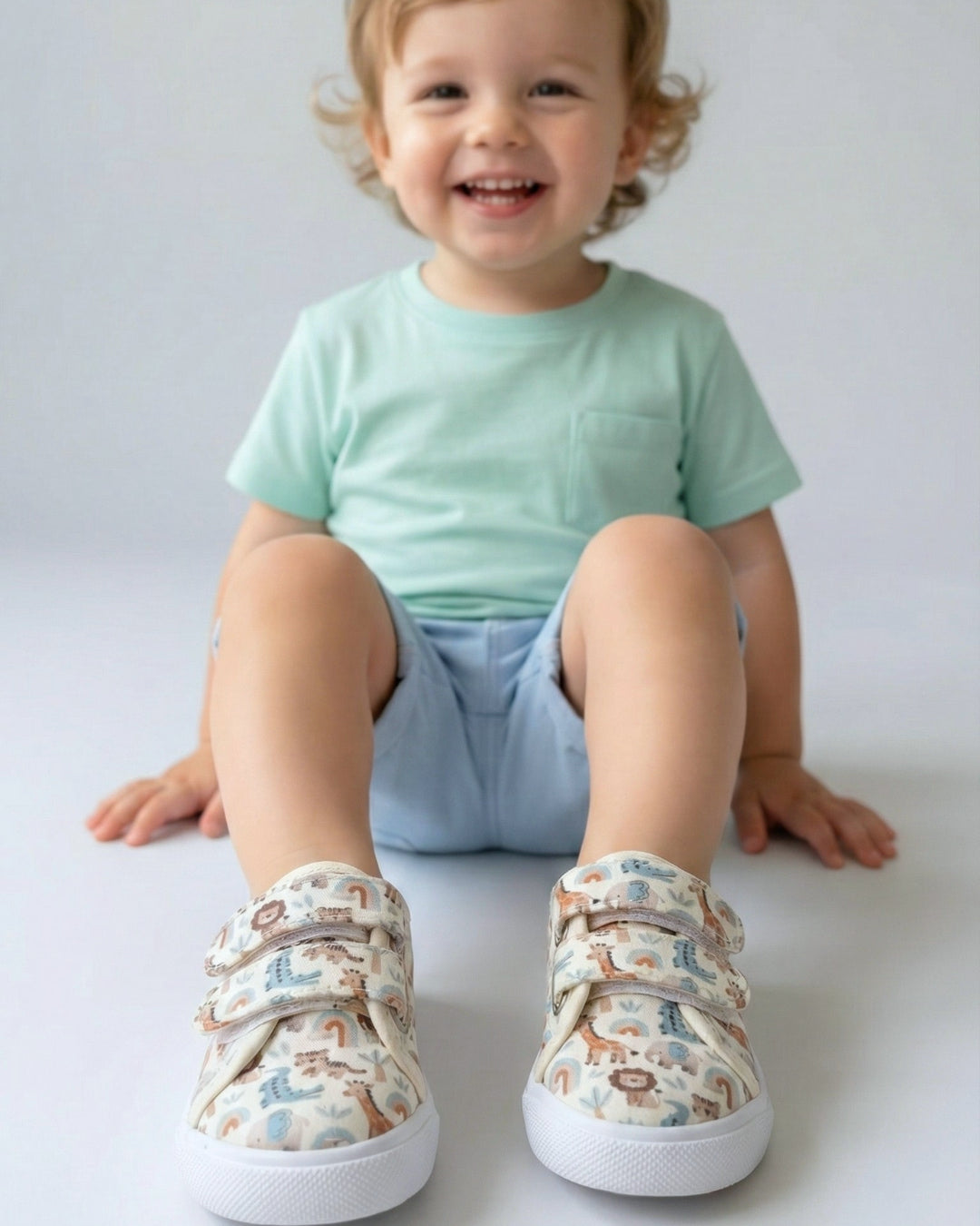 Child wearing light green shirt and patterned shoes sitting on a white surface
