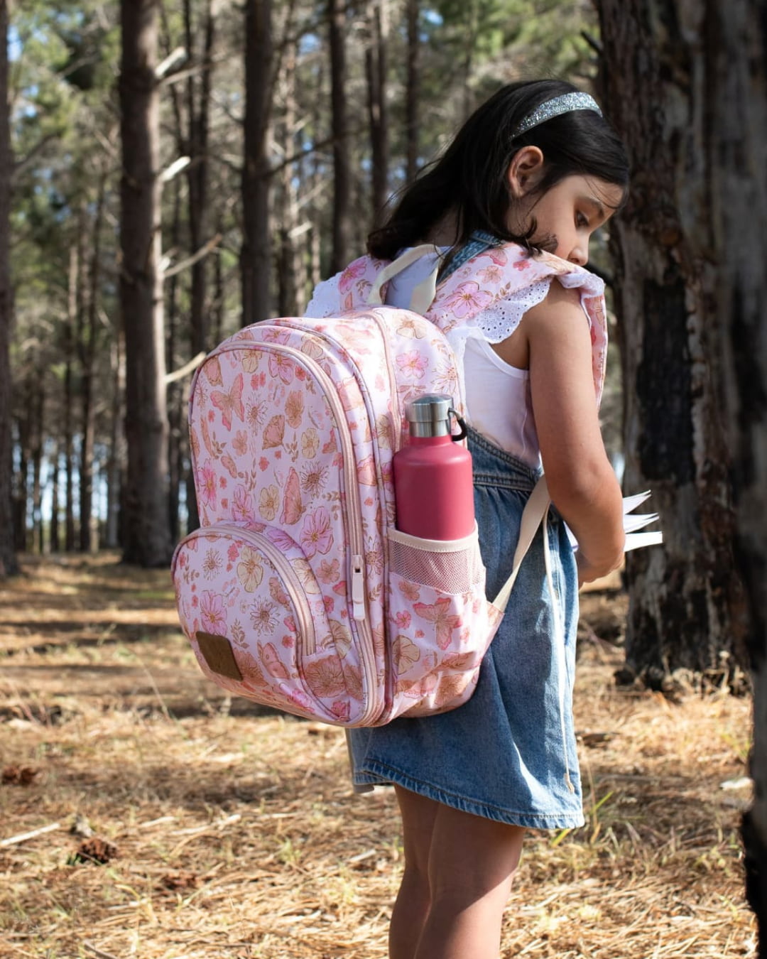 Girl wearing pink butterfly print small backpack with side pocket and bottle holder for school or nature walk.
