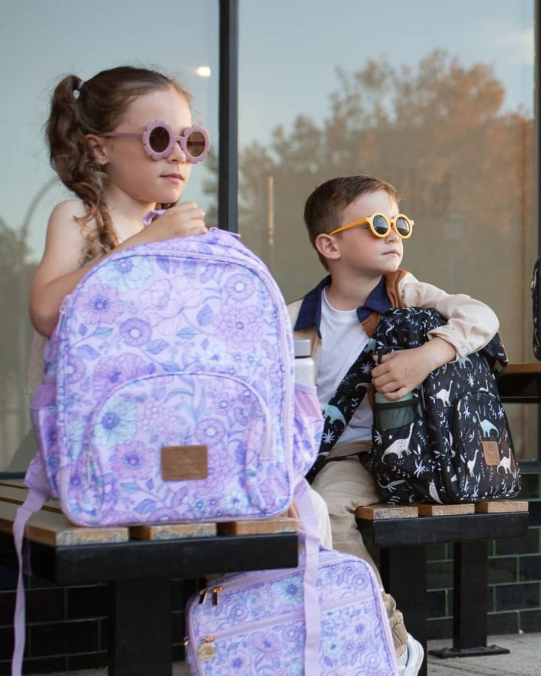 Stylish siblings with lilac floral and black dinosaur print small backpacks for school, day trips, and outdoor fun.