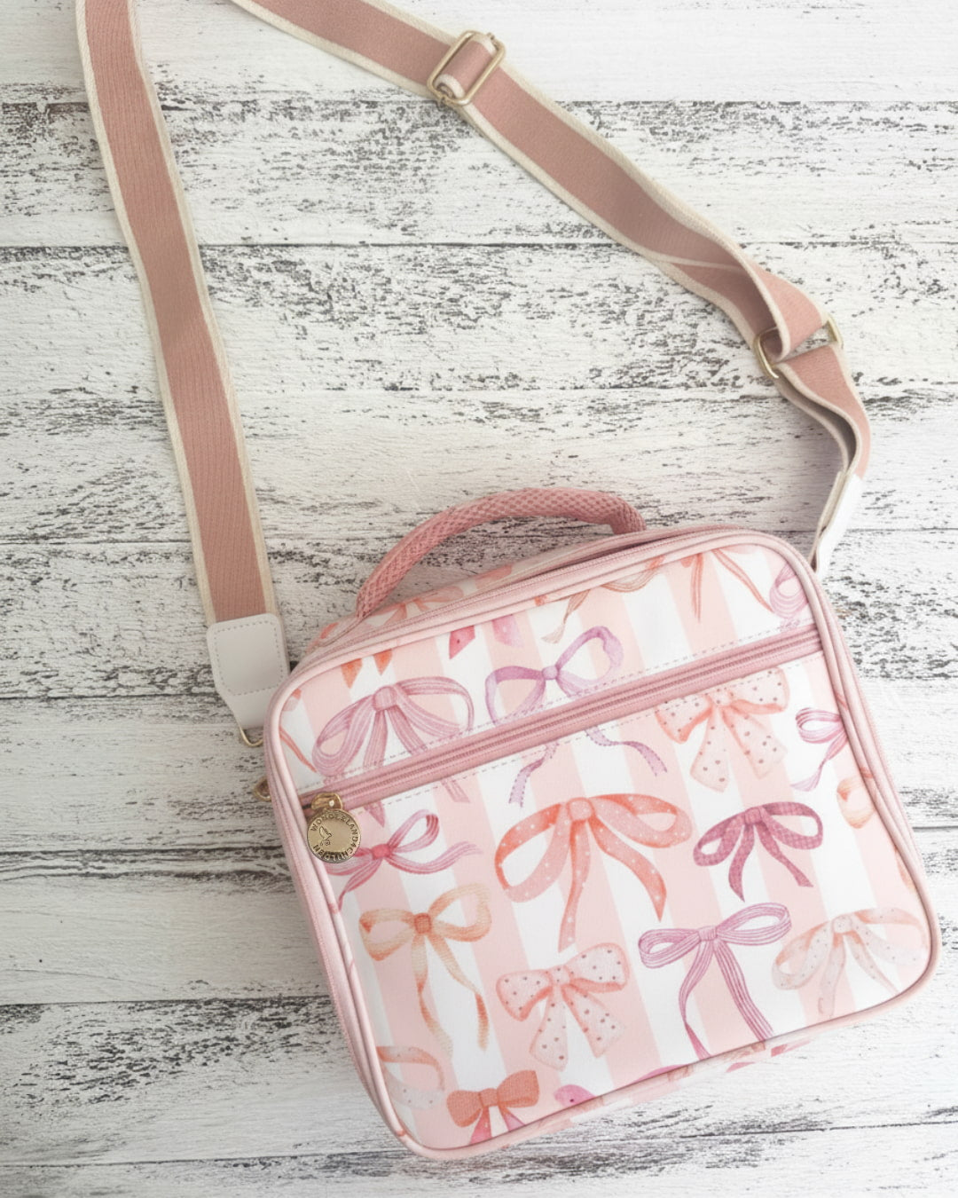 Pink crossbody bag with bow pattern on a wooden surface