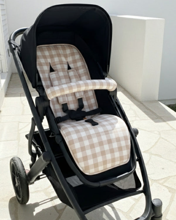 Black stroller with beige checkered seat cover on a tiled floor.