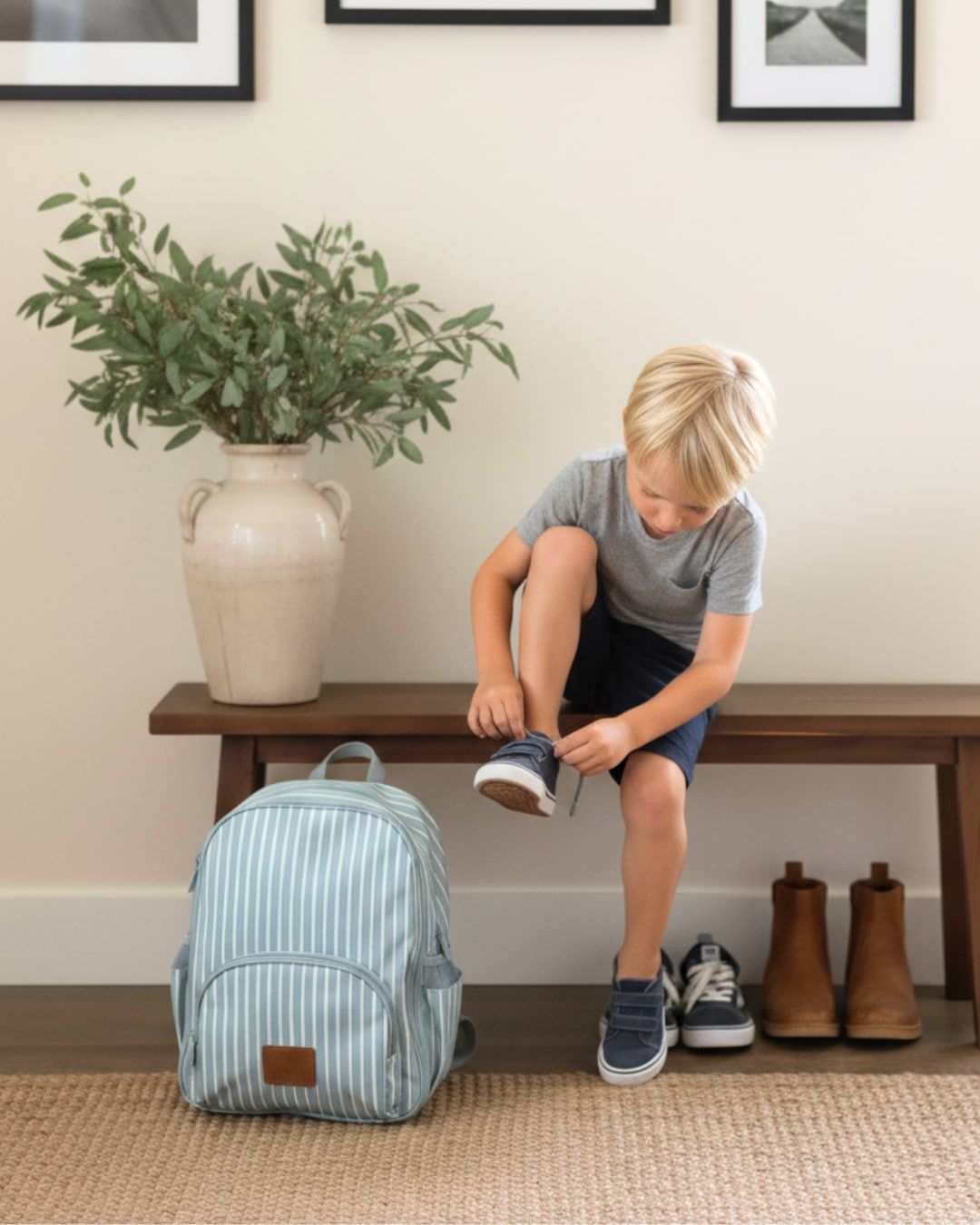 Child sitting on a bench tying shoes next to a striped backpack in a home setting.