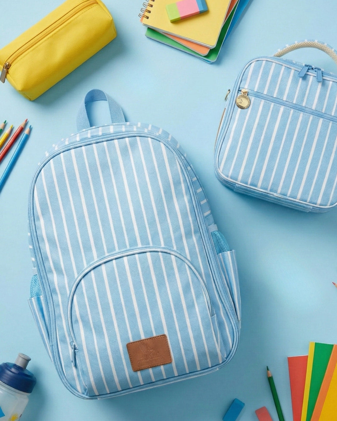 Striped backpack and lunch bag on a blue background with school supplies.