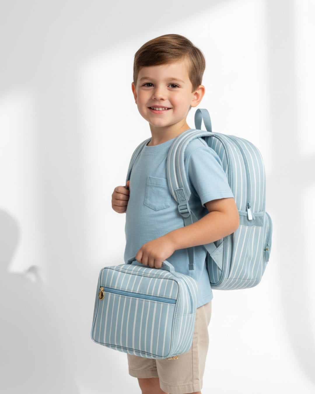 Child wearing a light blue backpack and holding a matching bag on a white background