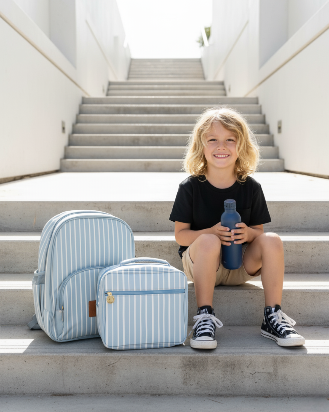 Child sitting on steps with striped backpack and blue water bottle