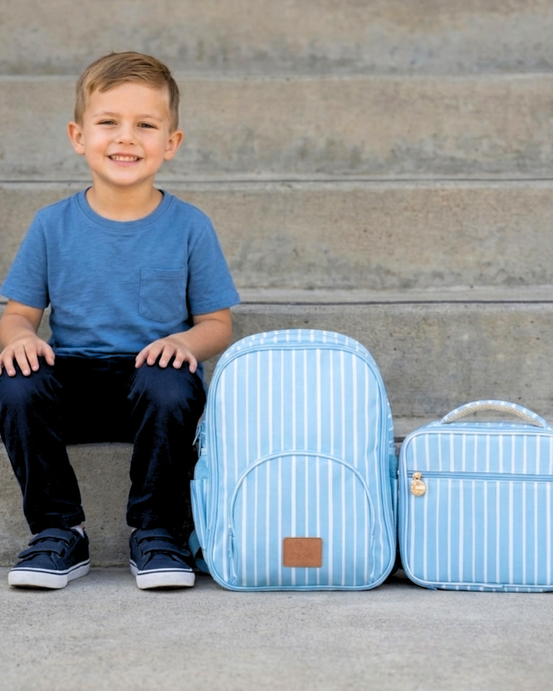 Child sitting on steps with a blue striped backpack and lunch bag