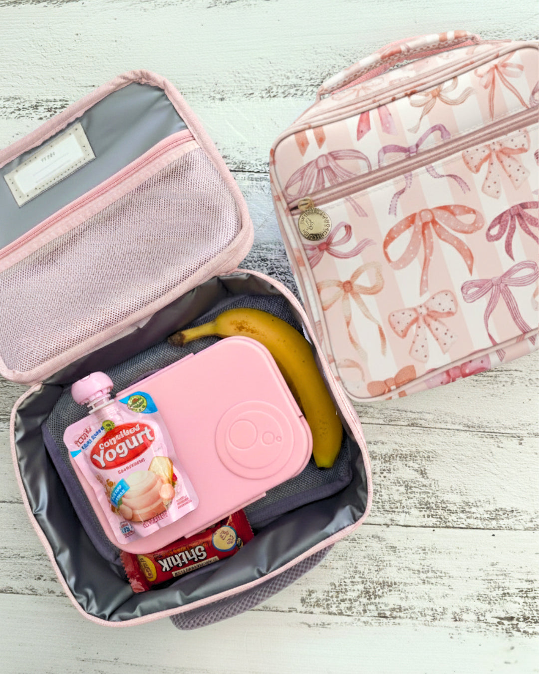Pink lunch box with yogurt, cookies, and a banana on a wooden surface