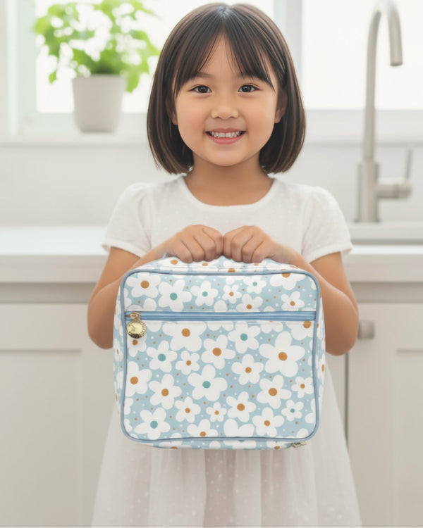 Child holding a floral-patterned lunch bag in a kitchen setting