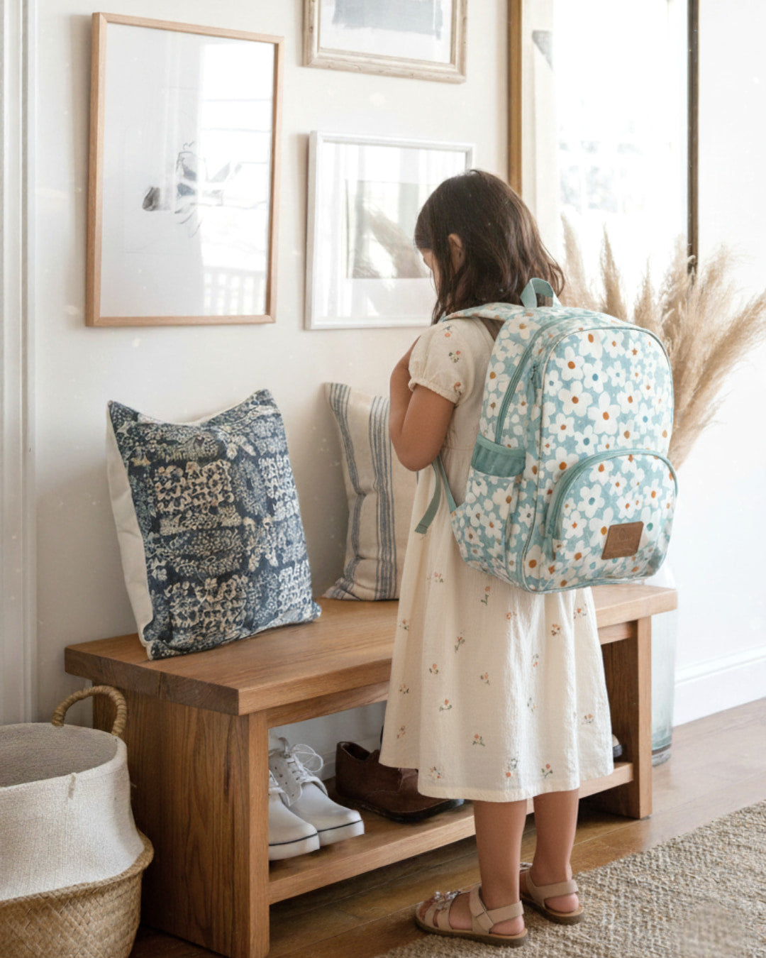 Child with a floral backpack standing next to a wooden bench in a home setting.