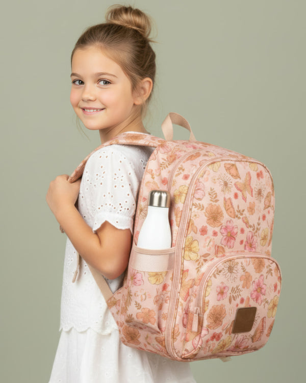 Young girl wearing a floral backpack with a water bottle, on a plain background
