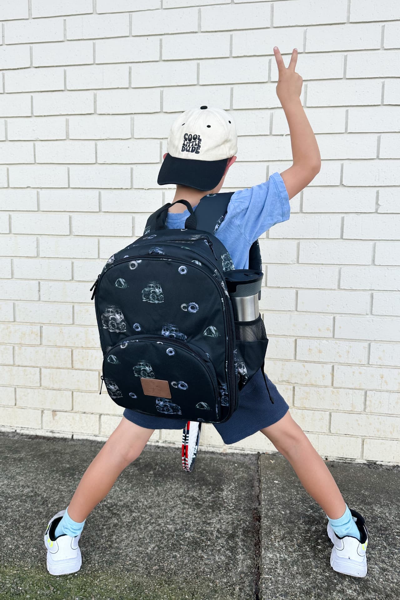 Primary school boy wearing black backpack with rugged truck and tire design