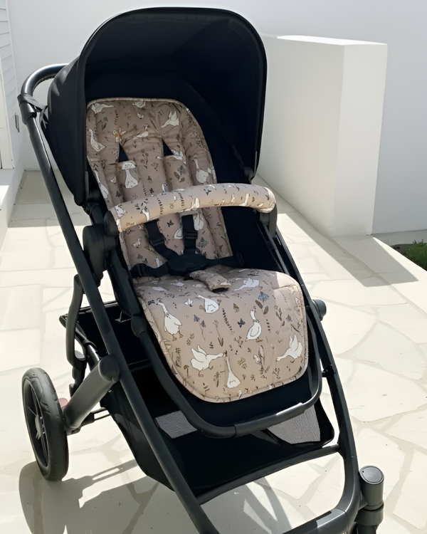 Black stroller with beige patterned seat cover on a light surface.