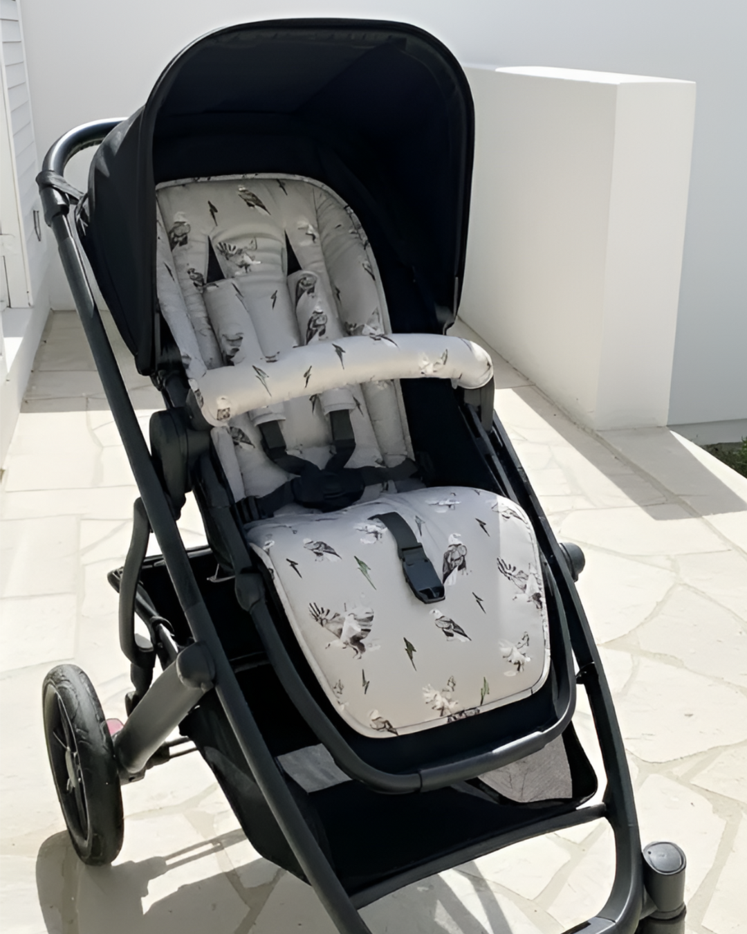 Black stroller with patterned seat and backrest on a tiled floor.