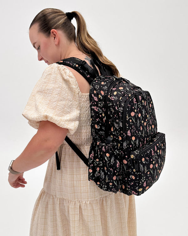 Woman wearing a black floral backpack on a white background