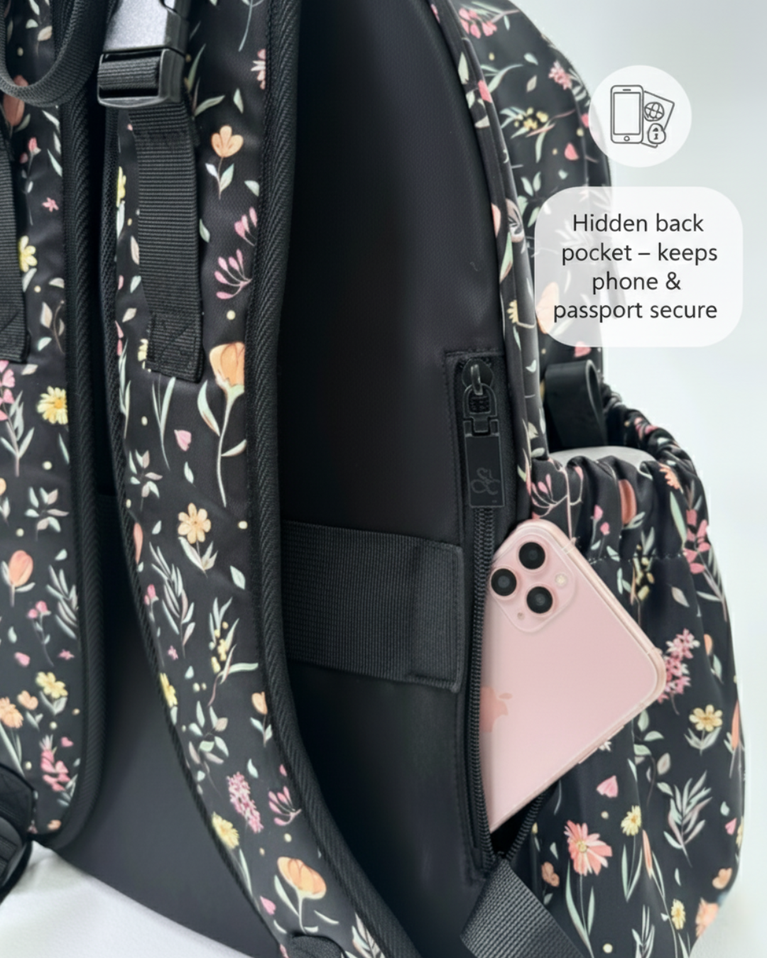 Floral-patterned backpack with a hidden back pocket holding a phone.
