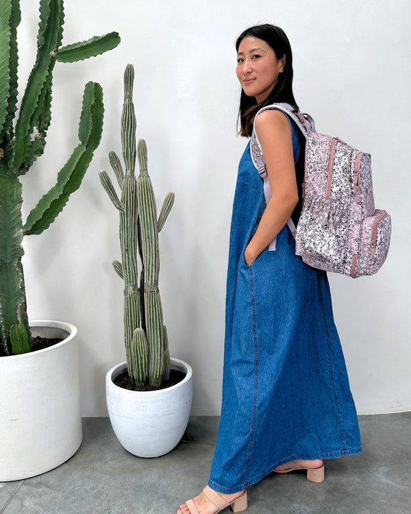 Woman in a blue dress with a pink sequin backpack standing next to potted cacti.