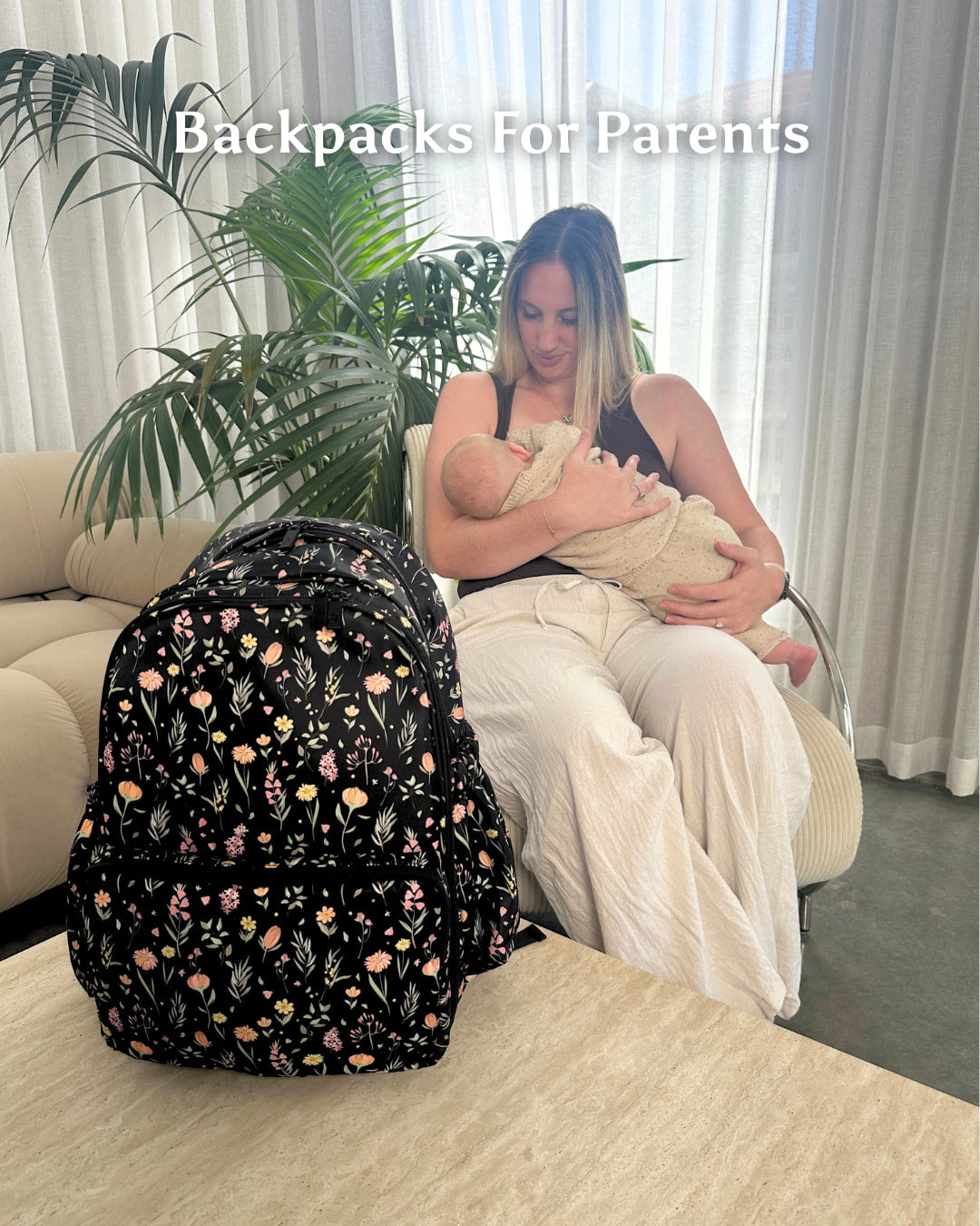 Woman holding a baby and sitting next to a floral backpack with text 'Backpacks For Parents'.