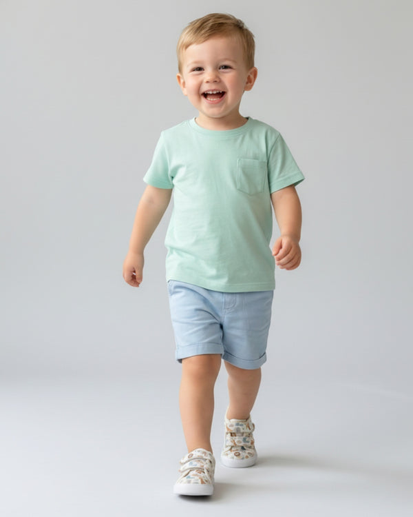 Child wearing a light green t-shirt and blue shorts on a plain background