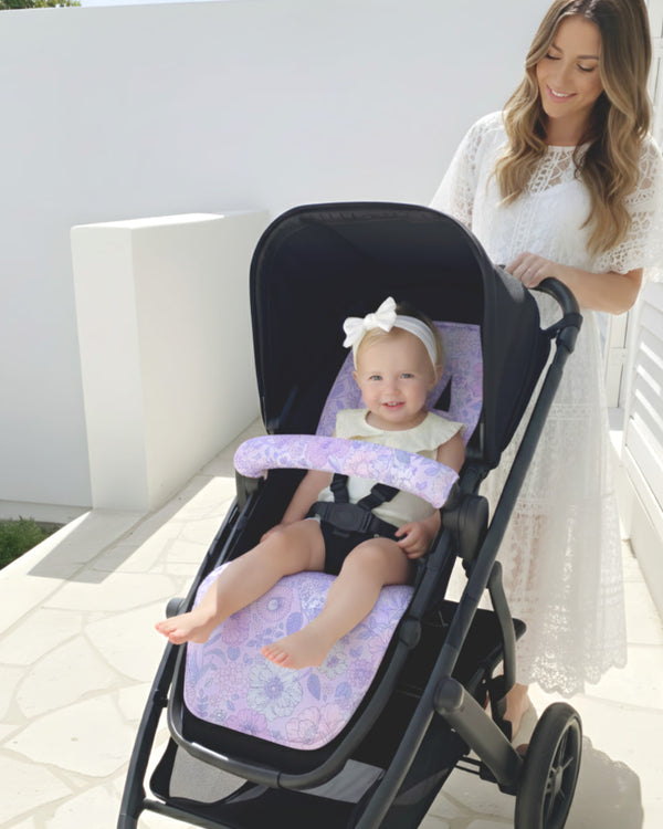 Woman pushing a stroller with a baby sitting inside on a sunny day.