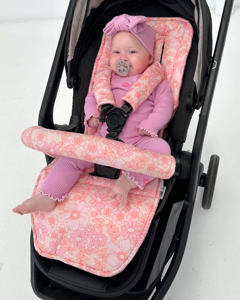 Baby in a stroller with pink floral seat cover on a white background