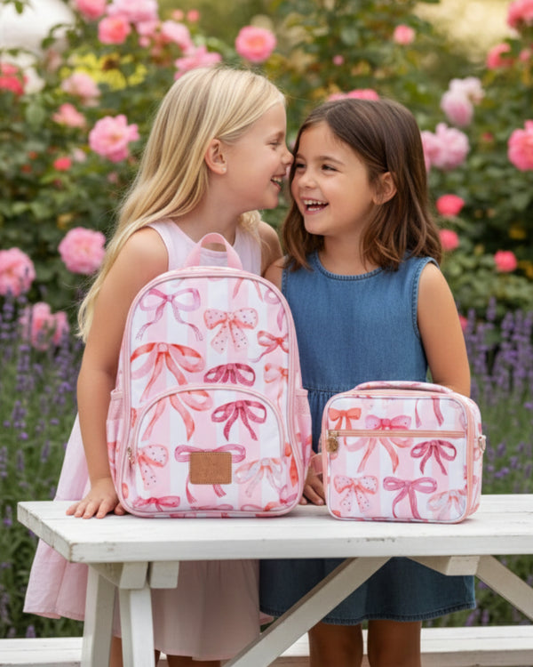 Two young girls with pink backpacks and lunch bags in a garden setting