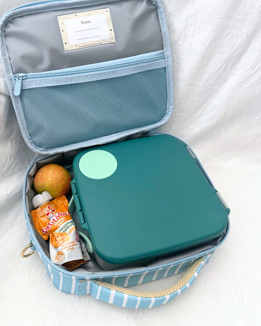 Open lunch box with compartments containing snacks and a fruit on a white background