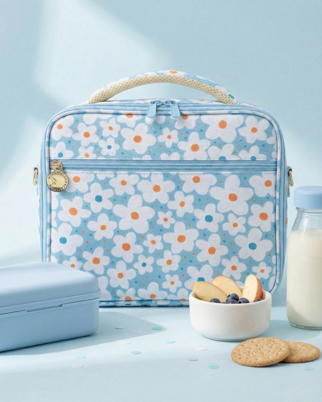 Floral-patterned lunch bag on a light blue background with a bowl of fruit and cookies.