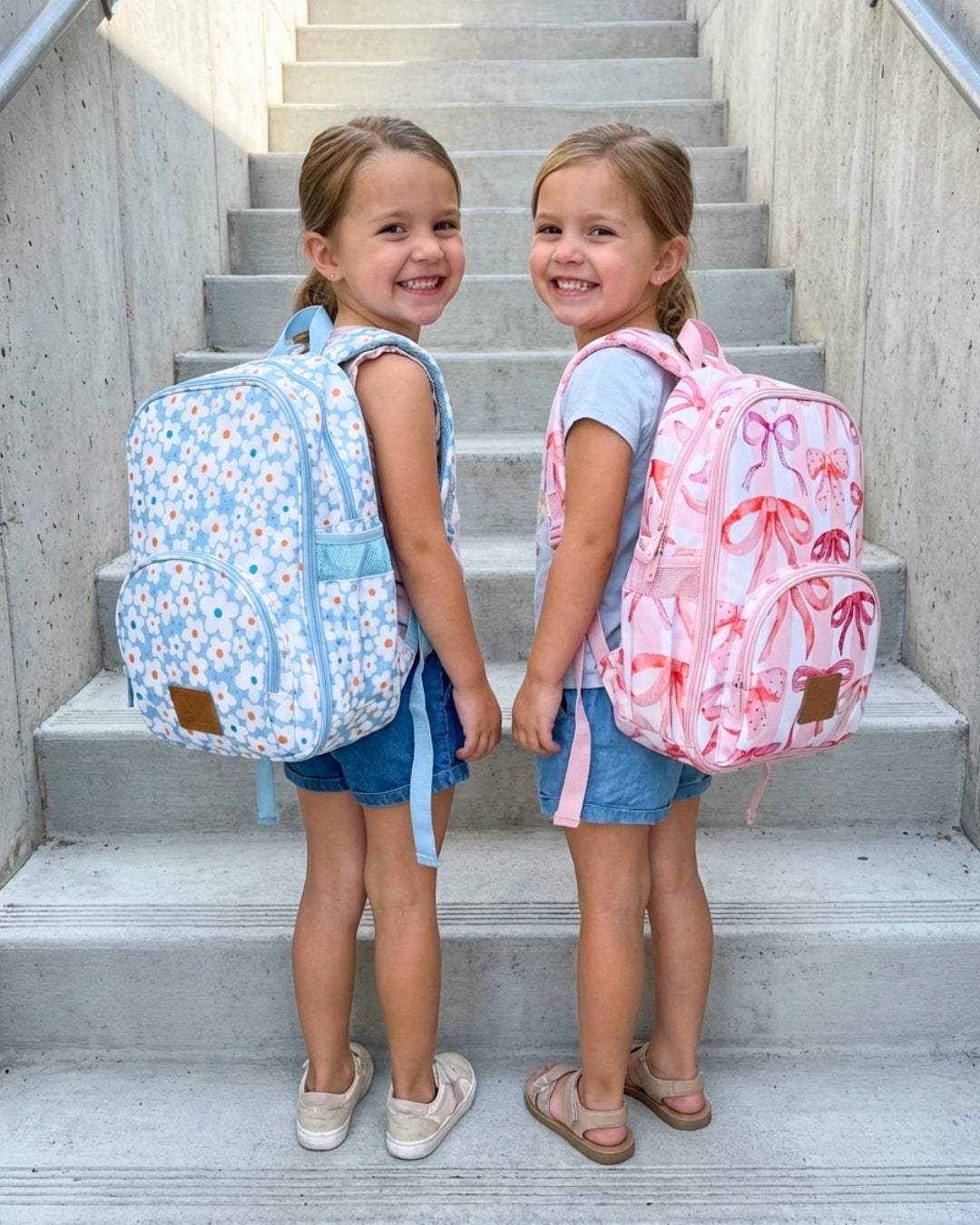 Two young girls standing on a set of stairs, wearing colorful backpacks.