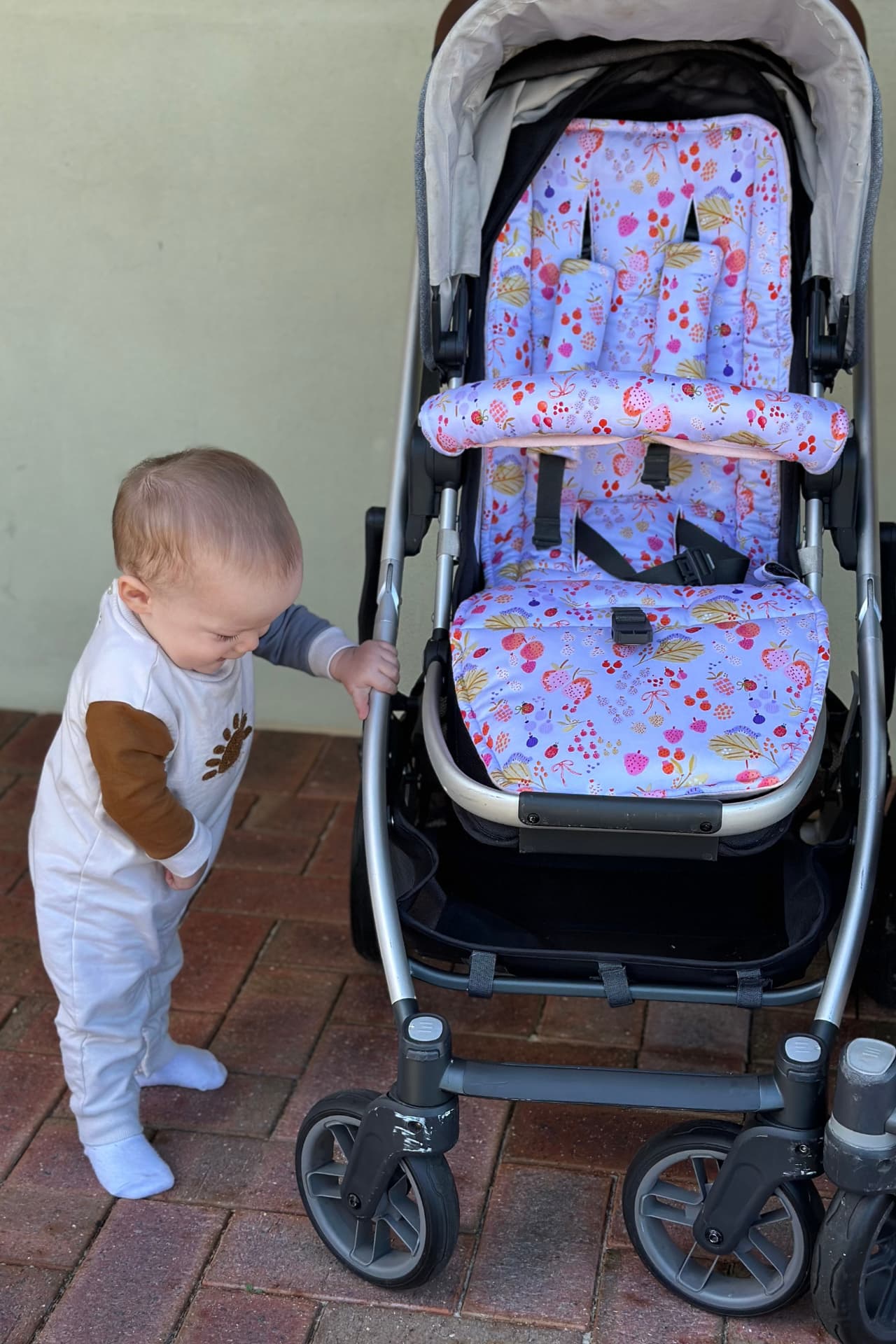 Child interacting with a stroller with a floral seat cover on a tiled floor.