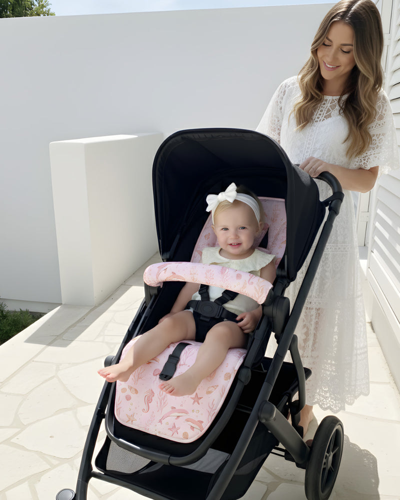 Woman pushing a stroller with a baby sitting inside on a sunny day.