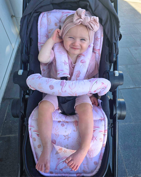 Child in a stroller with pink seat cover and headband, sitting on a tiled floor.