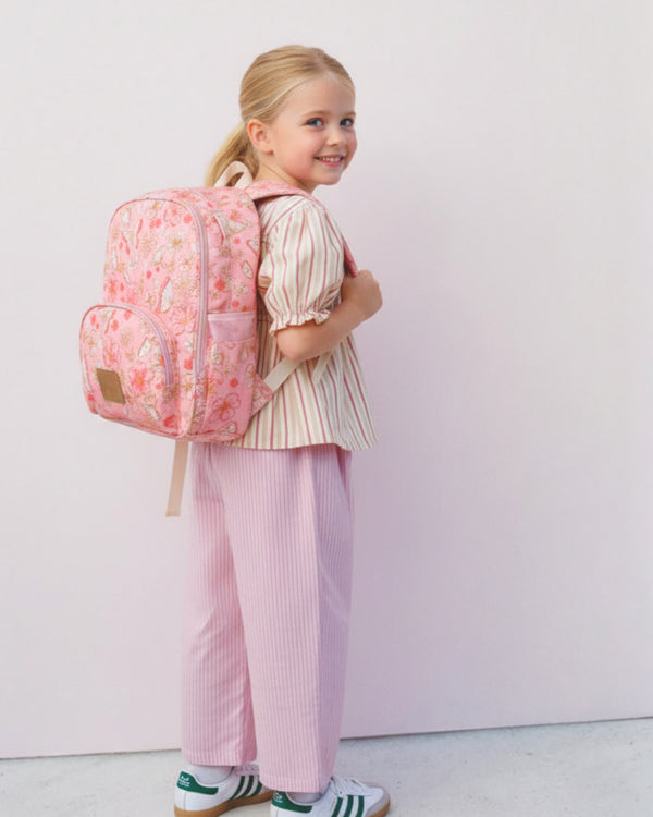 Young girl wearing a pink floral backpack against a white background