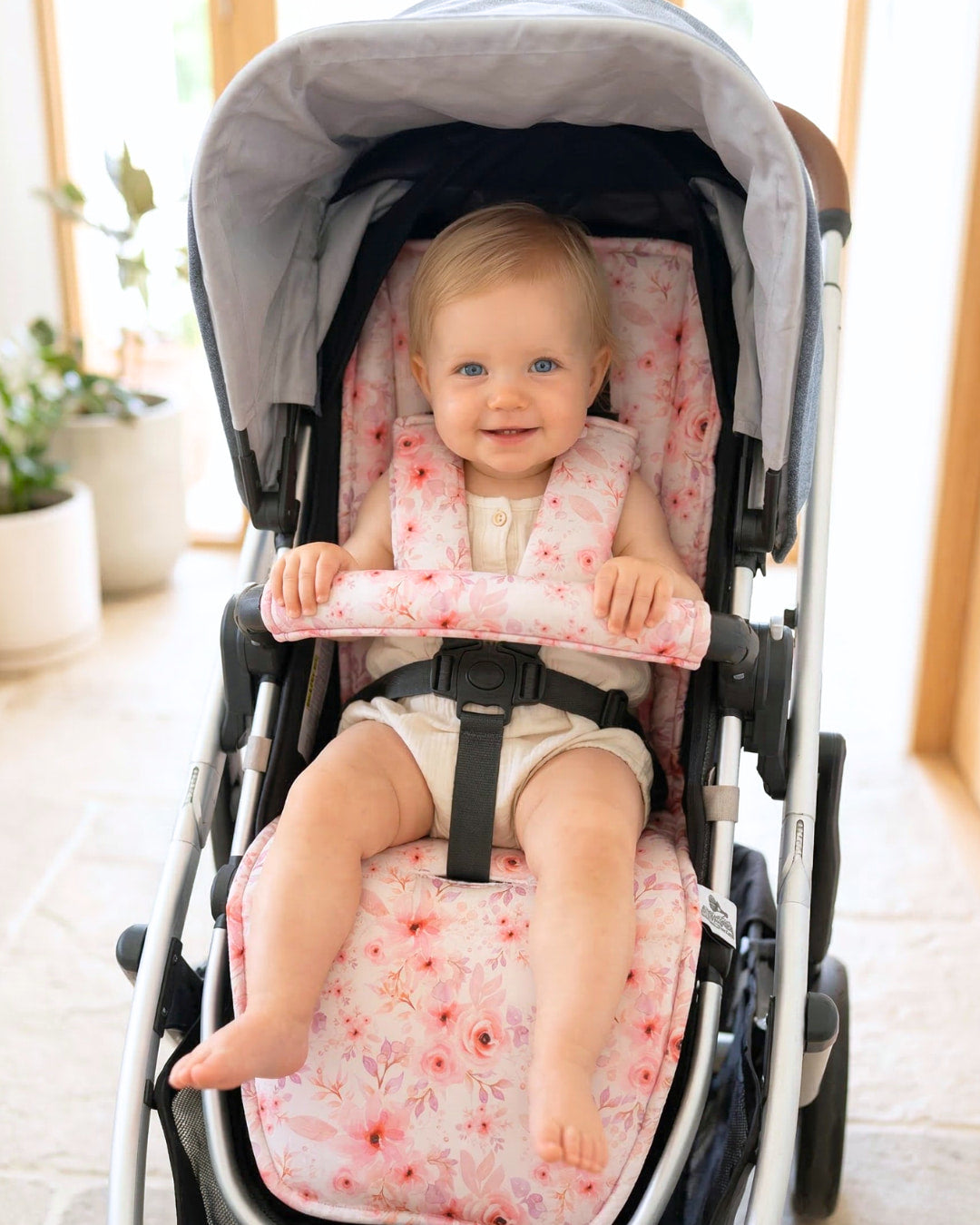 Baby sitting in a stroller with a pink floral stroller liner on a bright, indoor background
