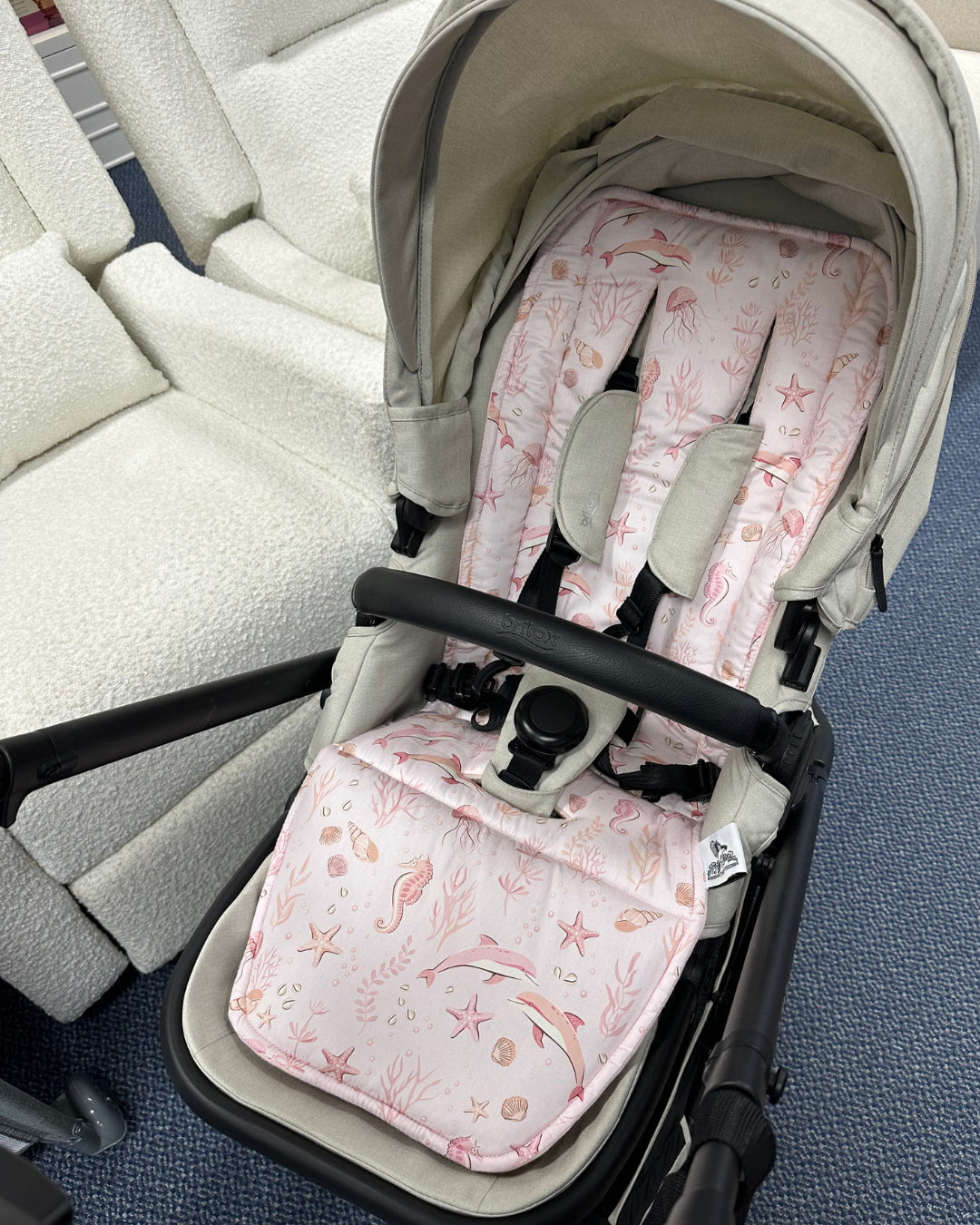 Baby stroller with pink and white patterned seat cover on a blue floor.