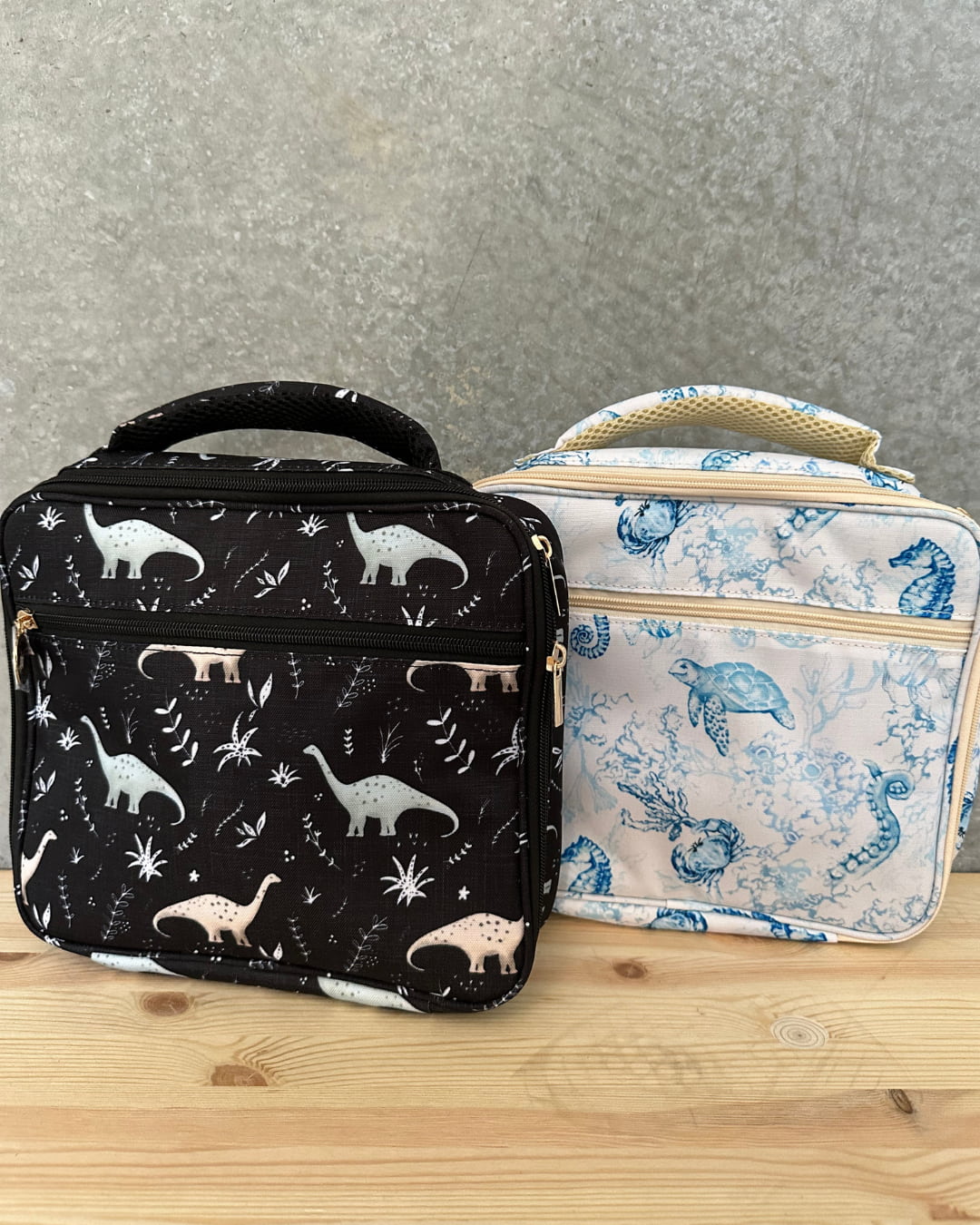 Two insulated lunch bags, one black dinosaur print and one blue ocean print, showing durable design for kids' school and travel meals.