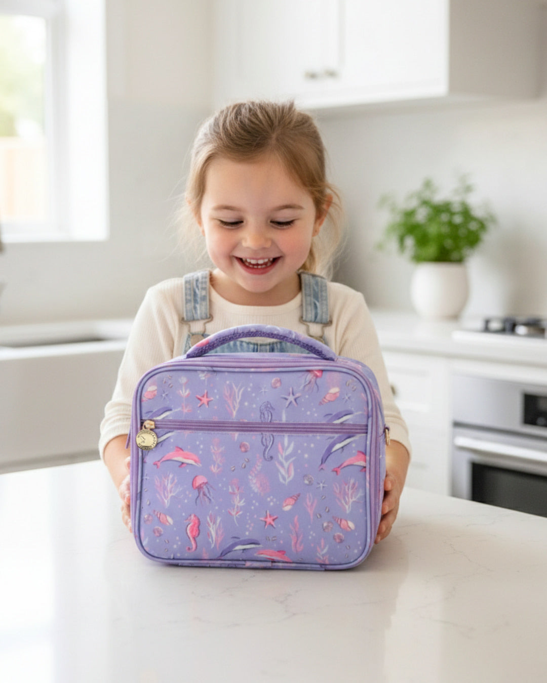 Young girl holding a purple lunch bag with floral design in a kitchen setting
