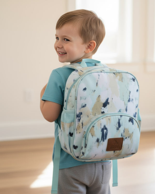 Child wearing a backpack with a light blue shirt and gray pants indoors.