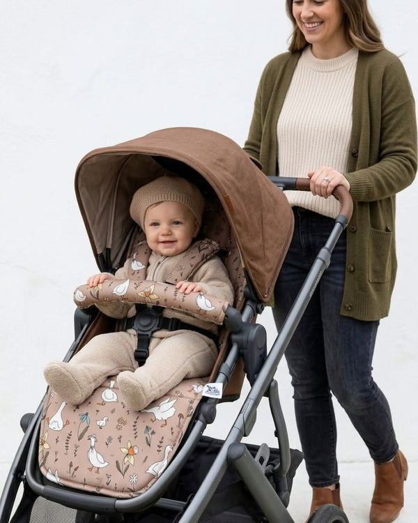 Woman pushing a baby in a stroller with a brown geese patterned pram  cover against a white background
