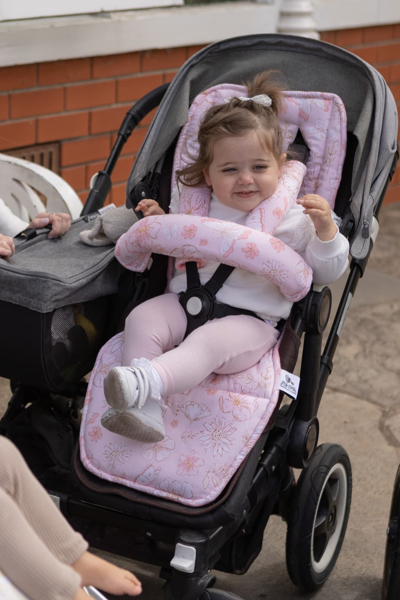 Child in a stroller with a pink floral seat cover on a sidewalk.