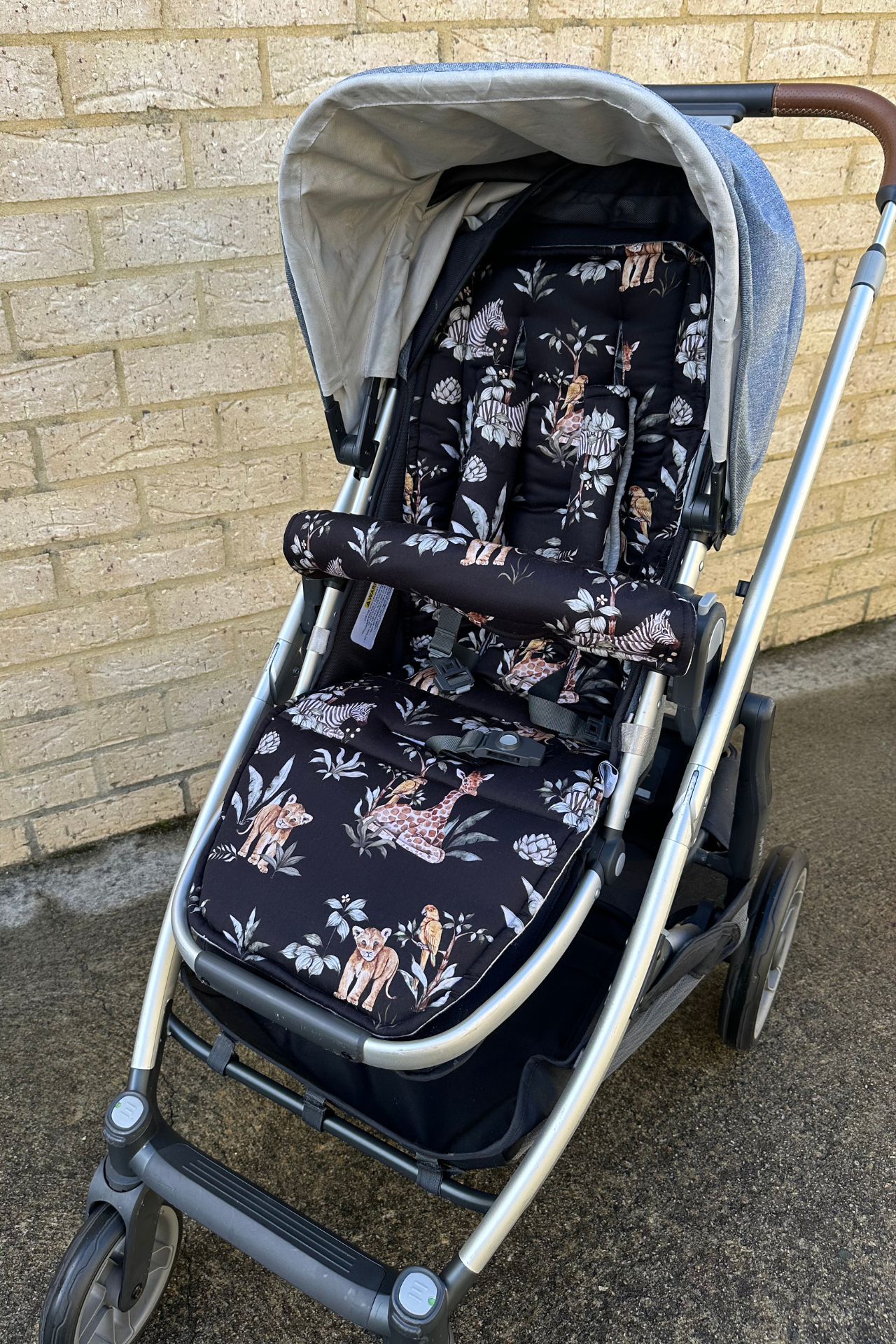 Stroller with safari animal patterned seat cover against a brick wall.