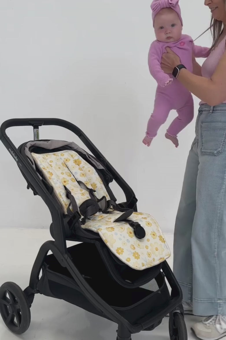 A mother demonstrates the easy installation of a universal pram liner, securing the five-point harness through the liner for a snug and safe fit for her baby.