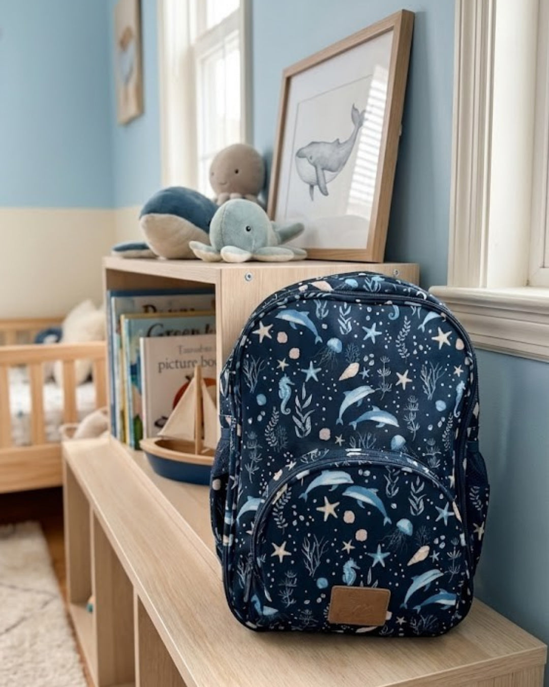 Navy blue backpack with sea-themed pattern on a wooden surface in a child's room.