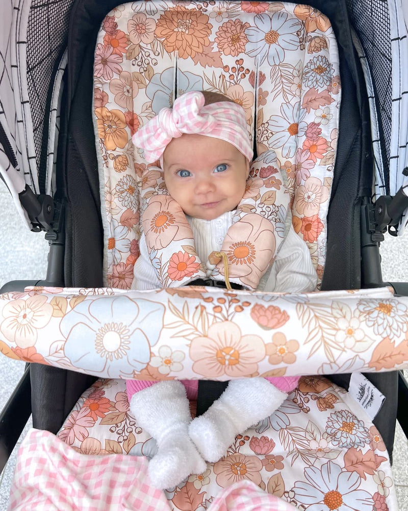 Baby in a floral car seat cover with a pink headband.