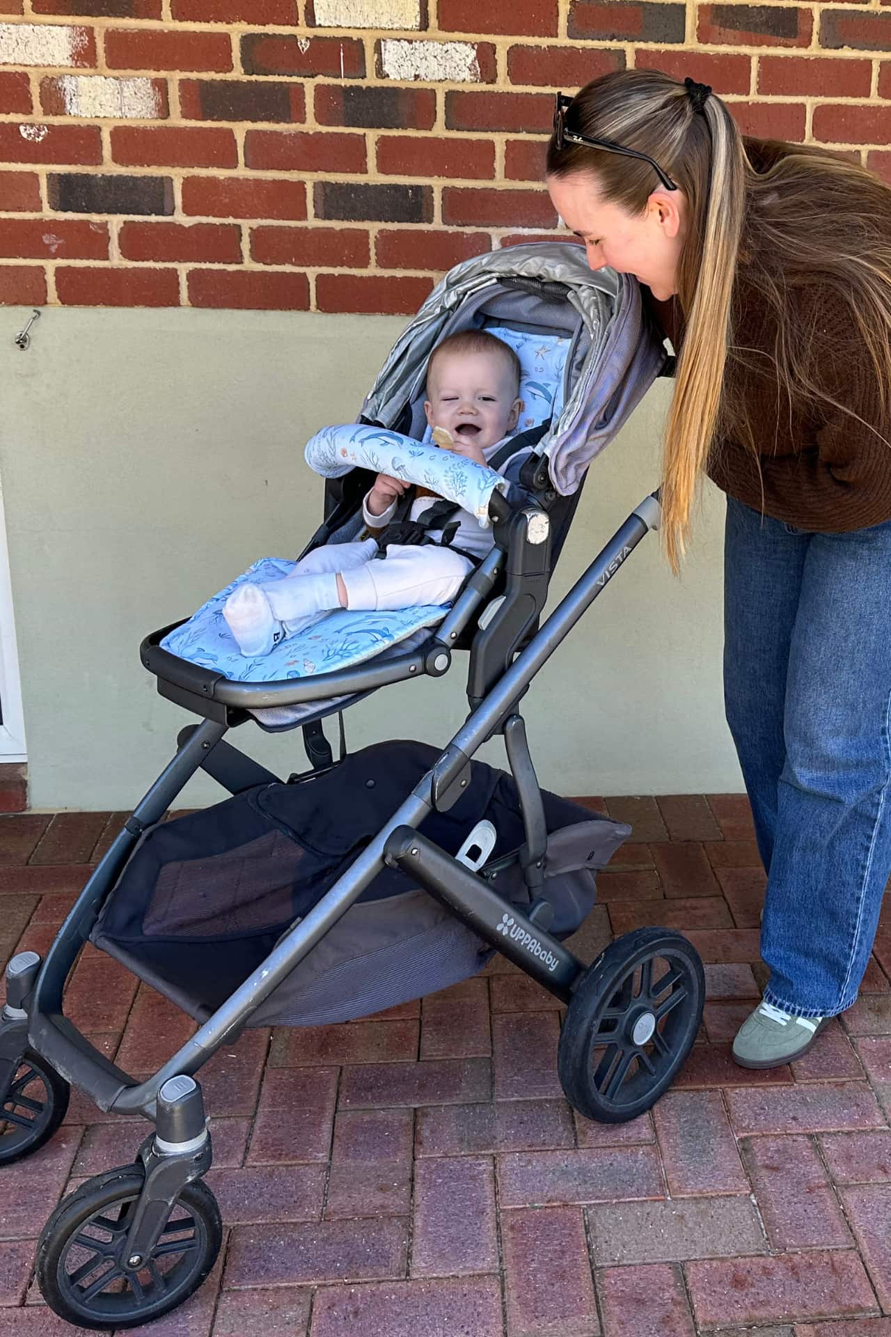 Woman with a baby in a stroller against a brick wall.